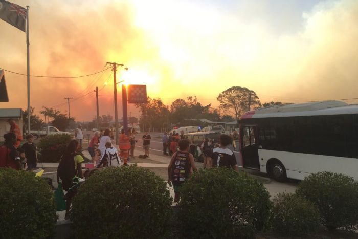 Residents standing at the police station with huge plumes of smoke in the background. 
