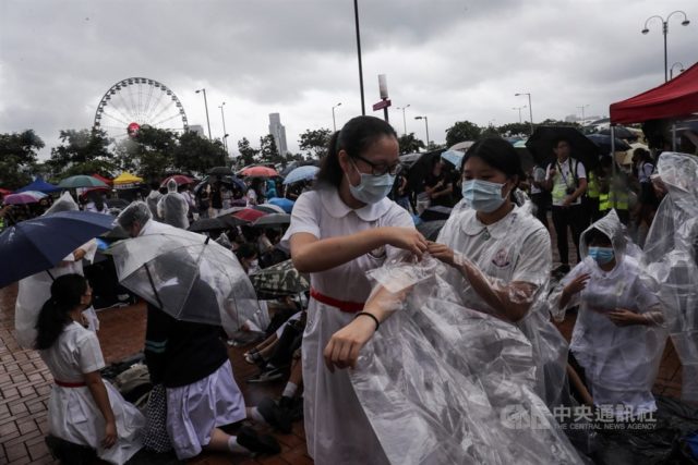 中学生在中环爱丁堡广场发起罢课集会，过程中雨越下越大，学生连忙穿起雨衣避雨。（图片来源：中央社）